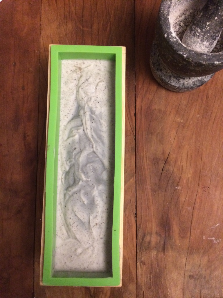 foto apresentando um pilão de pedra com resina de breu branco e uma barra de sabonete no molde de silicone durante o processo de formação da fase gel, poucas horas após o envase da massa, feito por processo a frio de sapoficação.